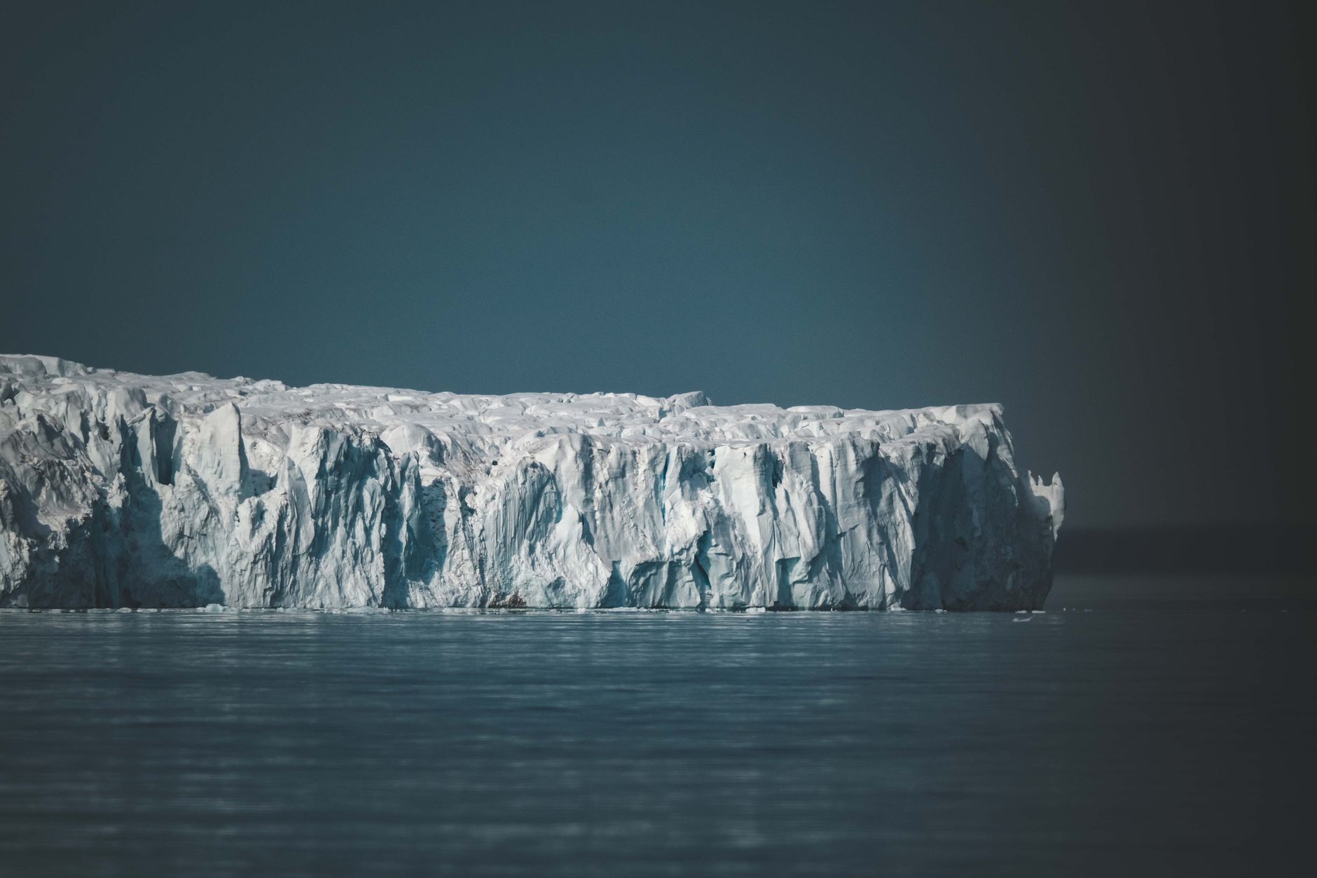 Massive tabular iceberg floating in calm Arctic waters under a pale blue sky