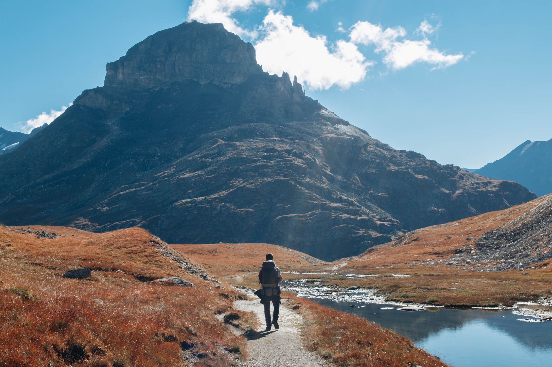 Hiker walking along a rocky trail through open highland terrain with peaks visible ahead