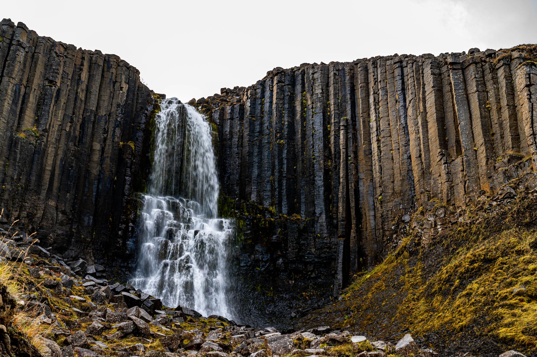 Waterfall cascading over dark volcanic basalt rock formation in a remote valley