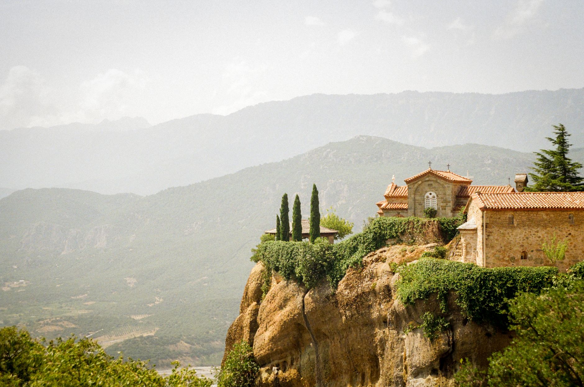 Remote stone monastery built into a sheer cliff face under a clear sky