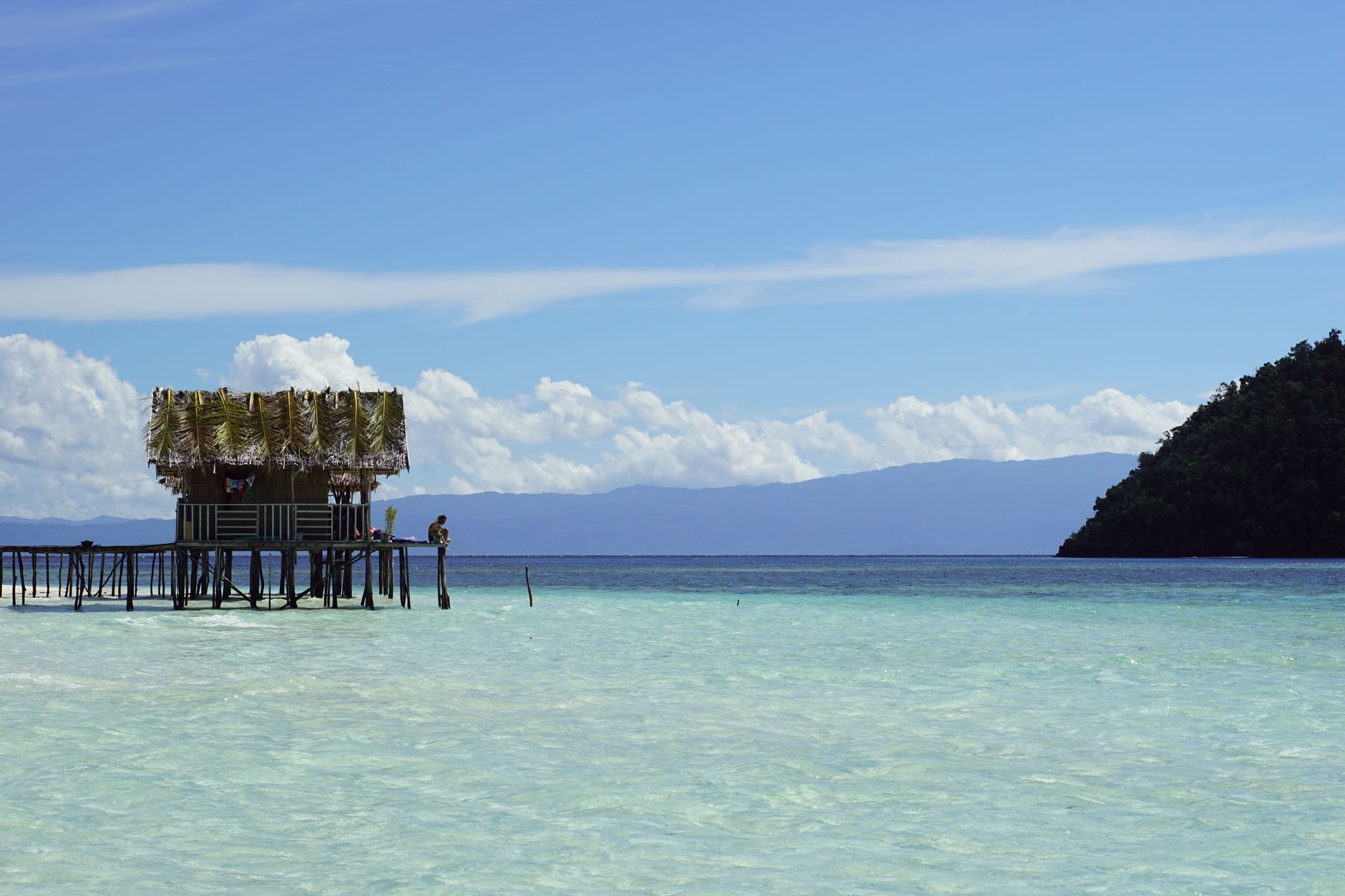 Wooden guesthouse built on stilts above calm turquoise water near a tropical island
