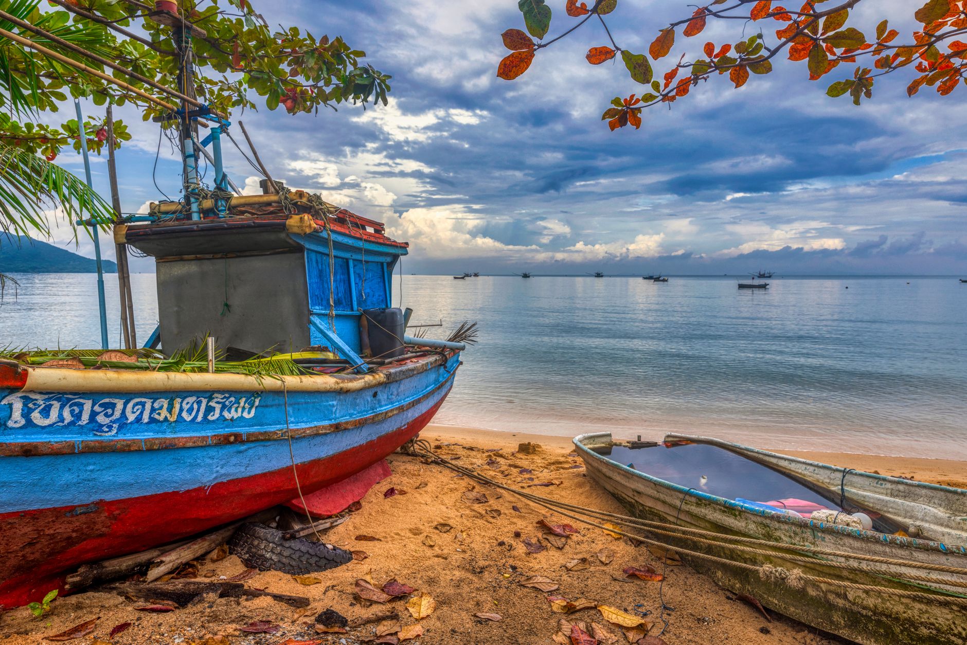 A small wooden boat crossing calm tropical waters toward a forested coastline