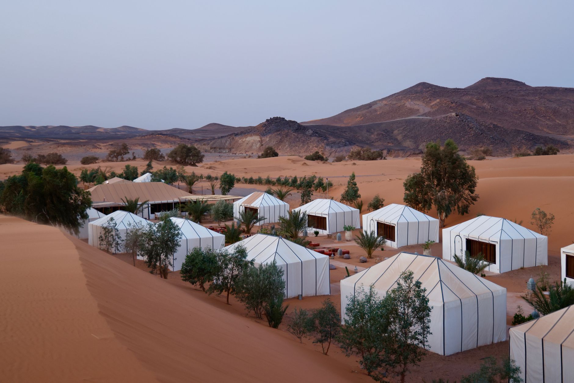 A small expedition camp with tents set up among sand dunes at dusk in a remote desert