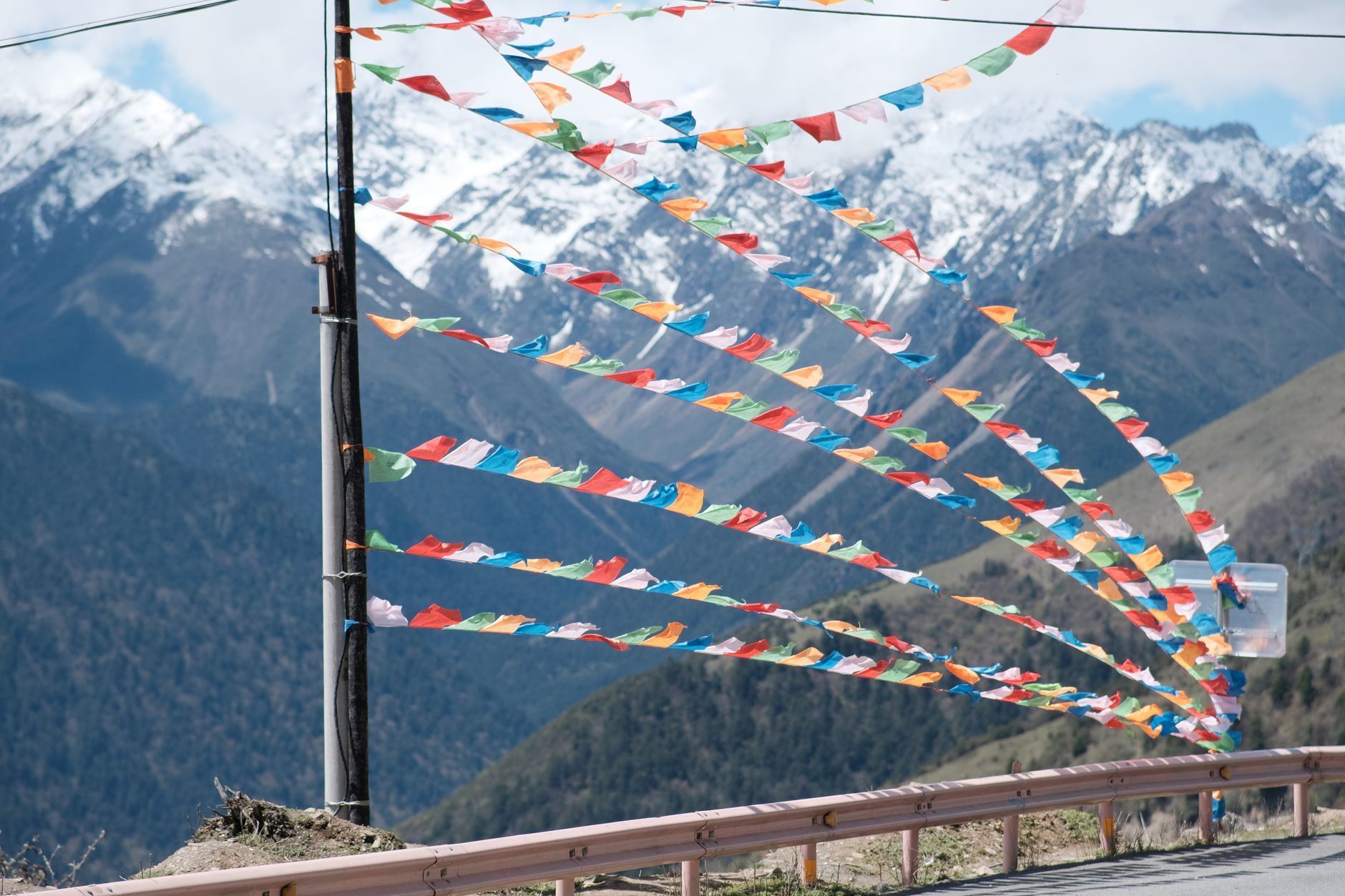 Colorful Tibetan Buddhist prayer flags strung across a high mountain pass with snow-capped peaks in the background