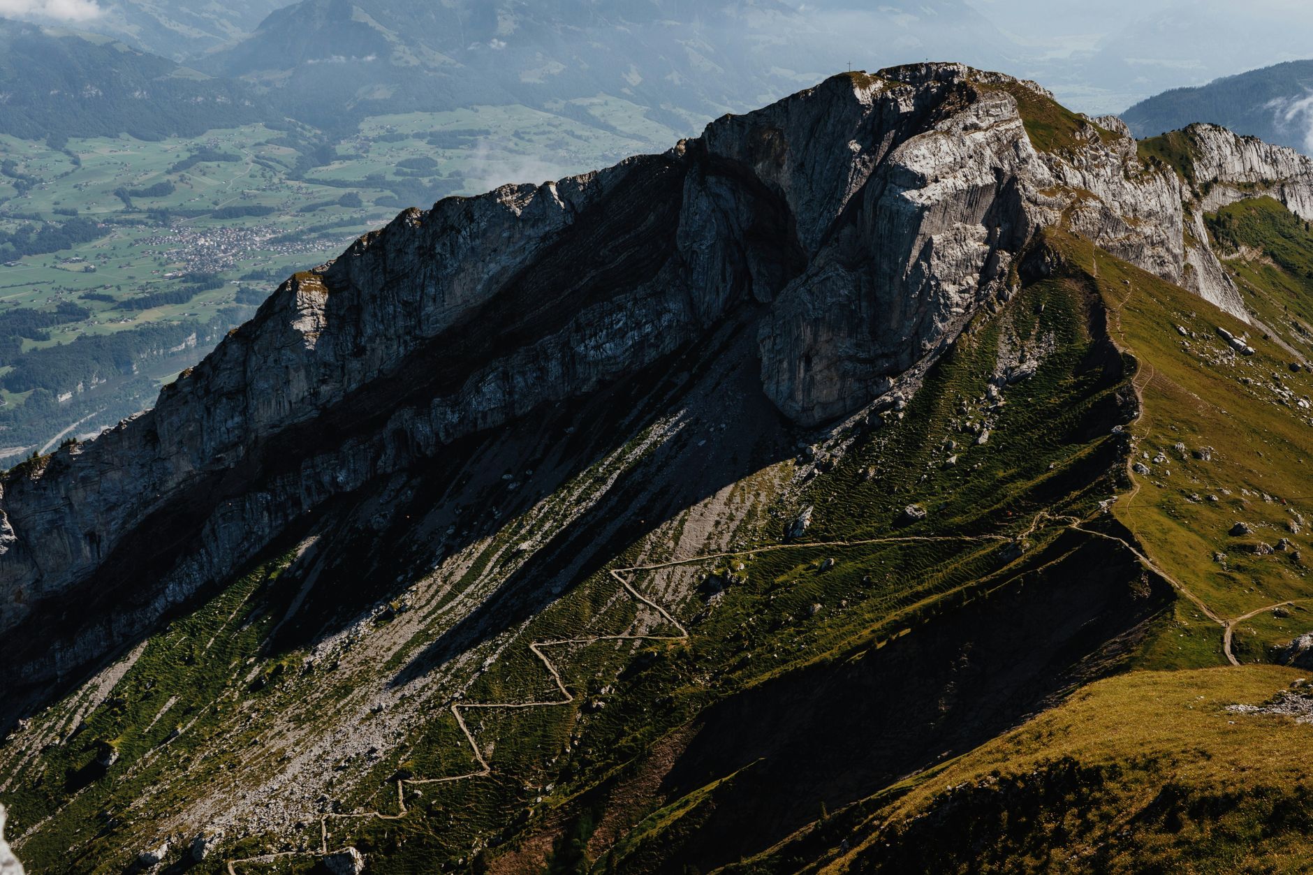 Hiker on a narrow alpine trail with dramatic mountain ridgelines in the background