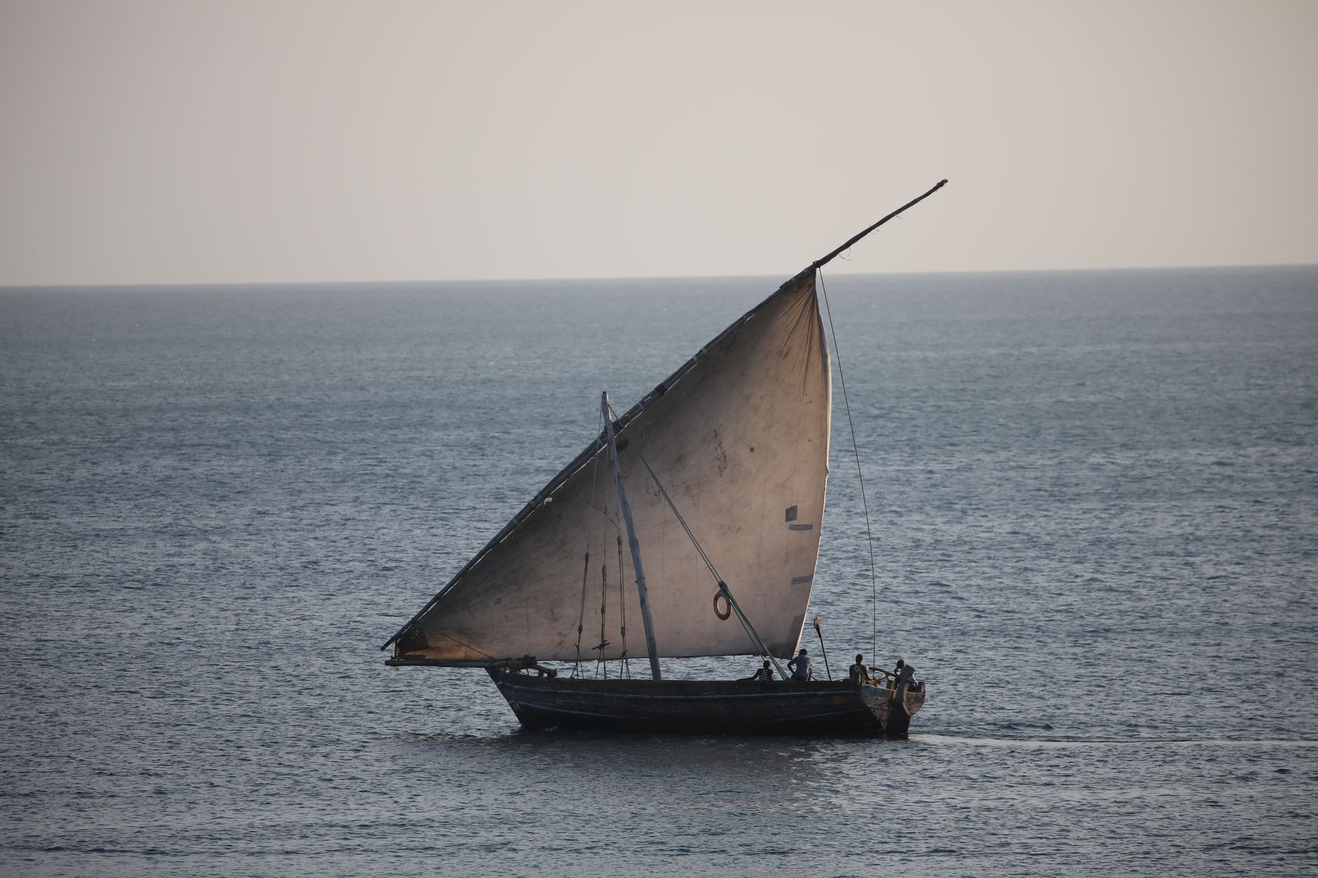 Traditional wooden dhow sailing on a large calm lake under clear sky