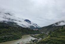 Wide green valley in Bhutan with traditional farmhouses and forested ridgelines in the background