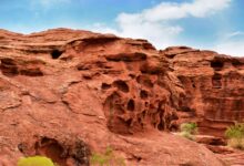 Red sandstone rock formations rising from a green meadow in Central Asia