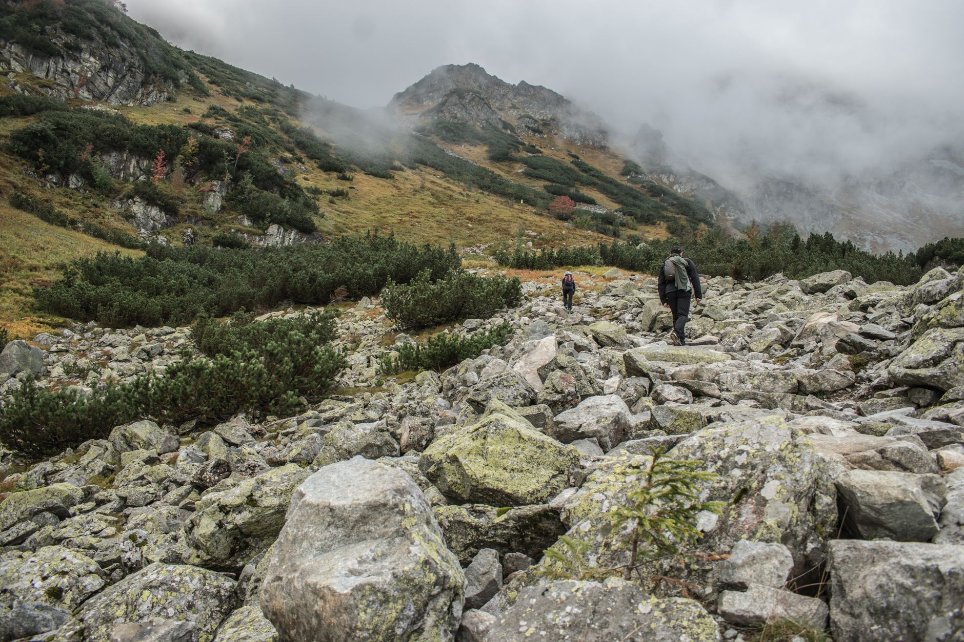 Hiker on a rocky mountain trail with dramatic peaks and open sky in the background