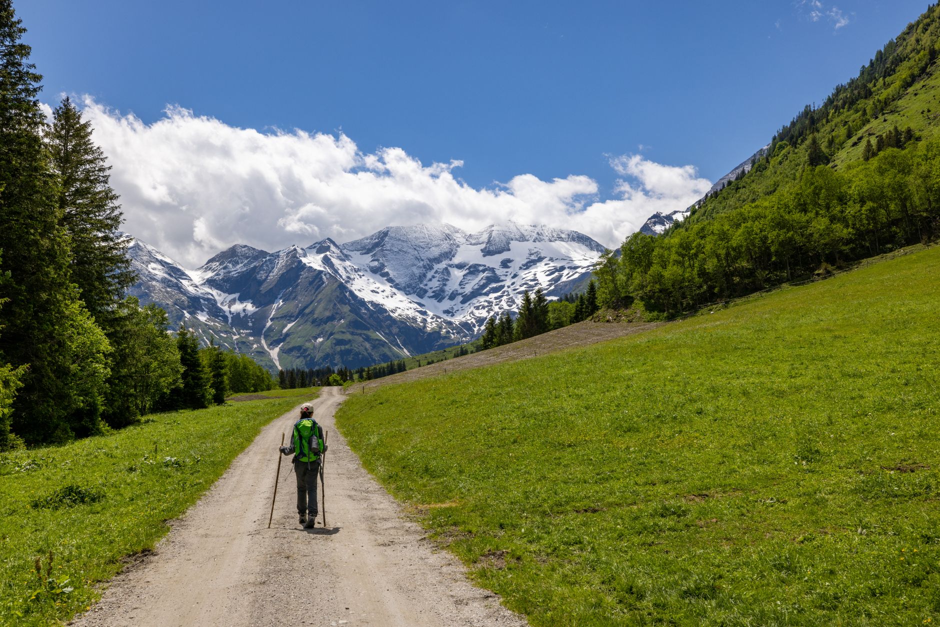 Hiker walking along a narrow mountain trail through high-altitude meadows with dramatic ridge lines in the background