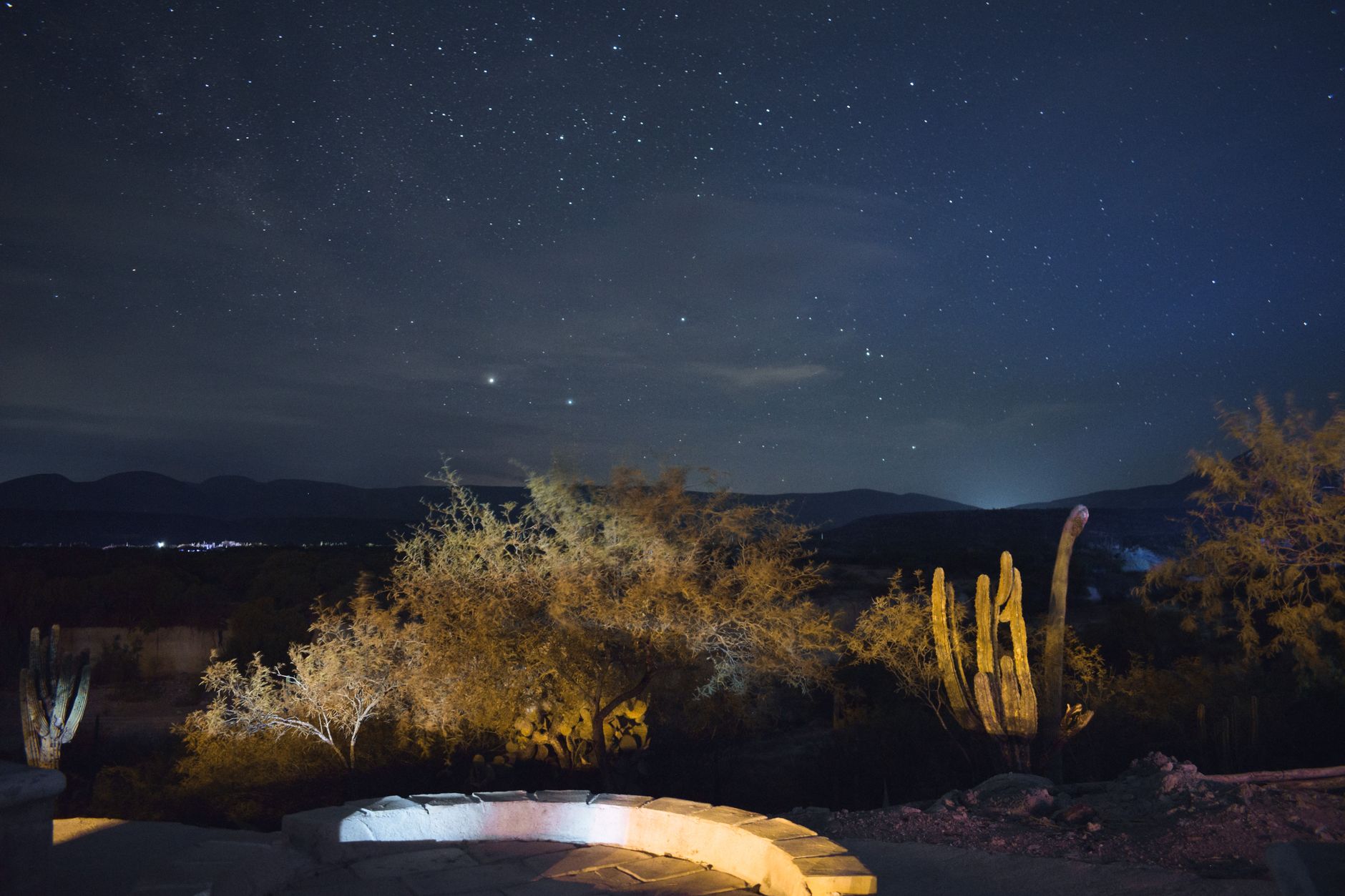 Milky Way visible over a dark desert landscape with silhouetted rock formations in the foreground
