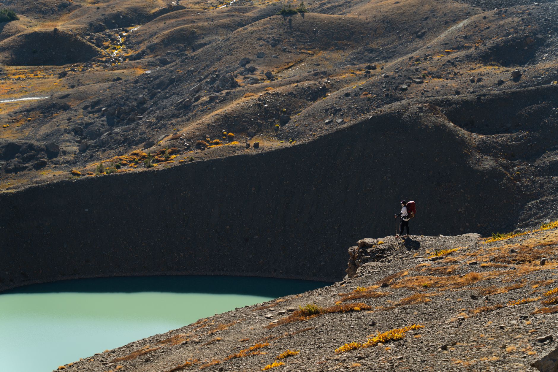 Solo hiker standing at the edge of a high-altitude crater lake in the Andes mountains