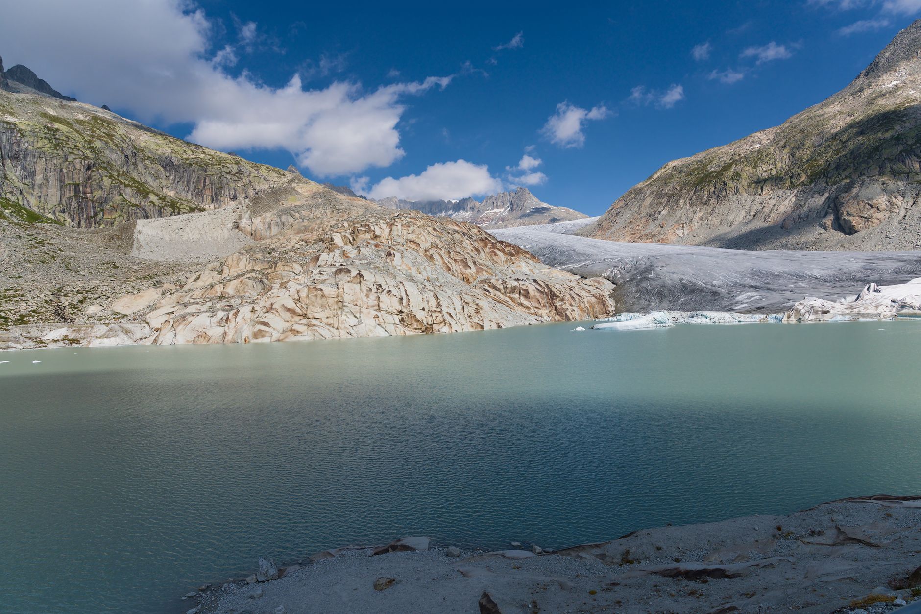 Still glacial lake surrounded by rocky alpine terrain under a blue sky