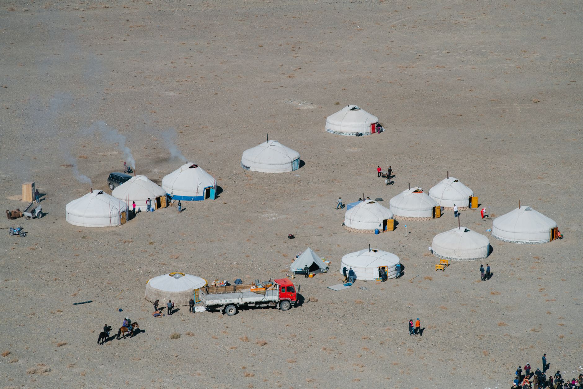 A traditional yurt camp on a high-altitude plateau surrounded by snow-capped mountain peaks