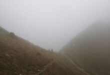 A narrow hiking trail disappearing into dense mist on a green mountain ridge