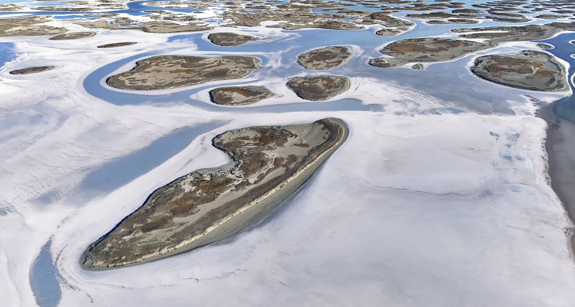 Aerial view of a white salt lake surrounded by volcanic rock in a desert landscape