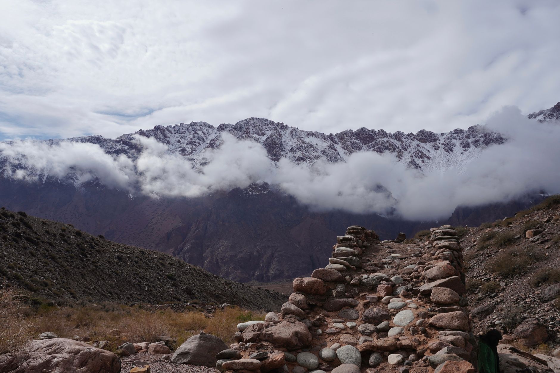 Hiker on a high-altitude trail through open Andean grassland with mountain peaks in the background