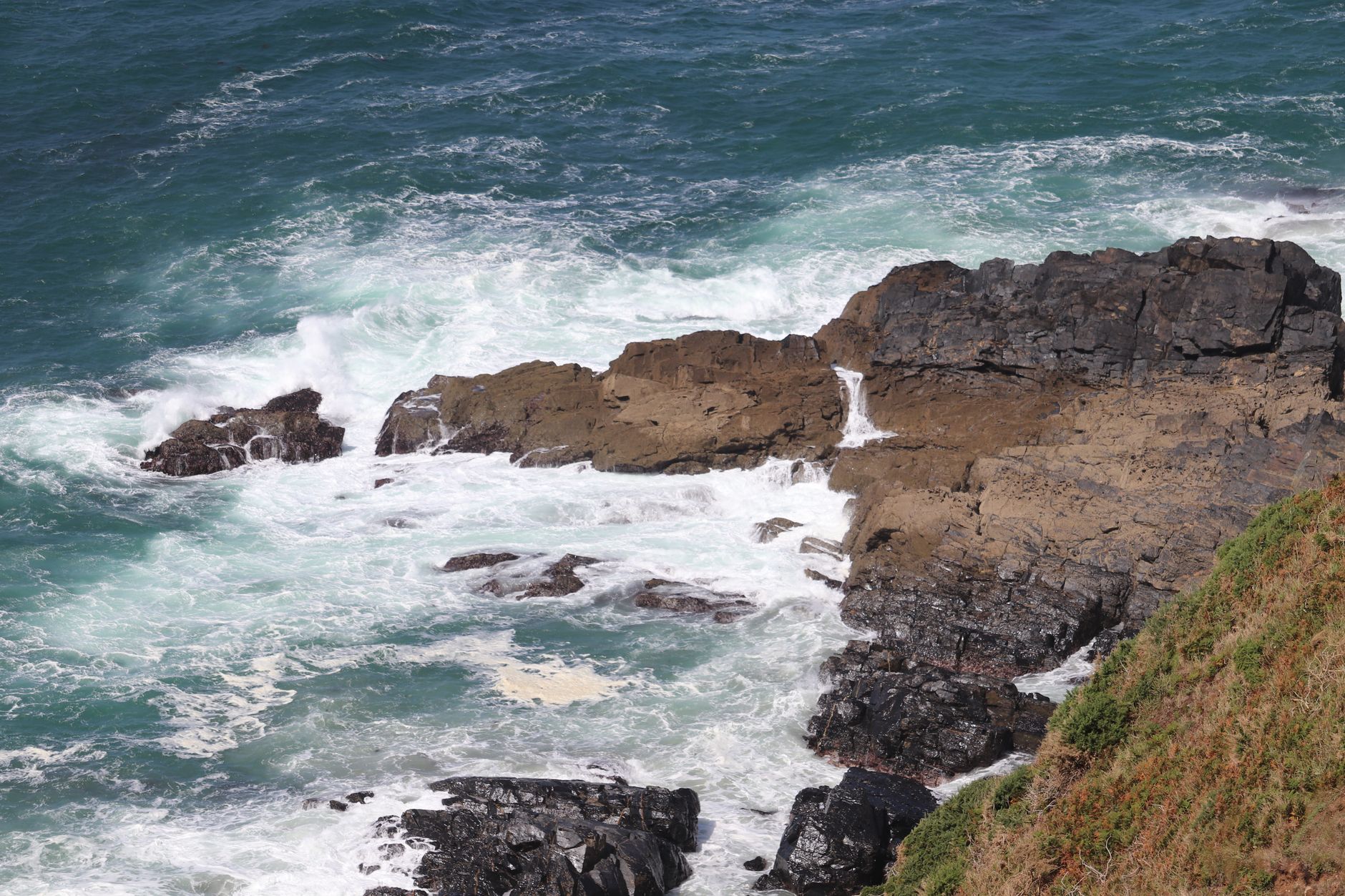Rocky coastal cliffs with heavy surf crashing below during monsoon season in southern Oman