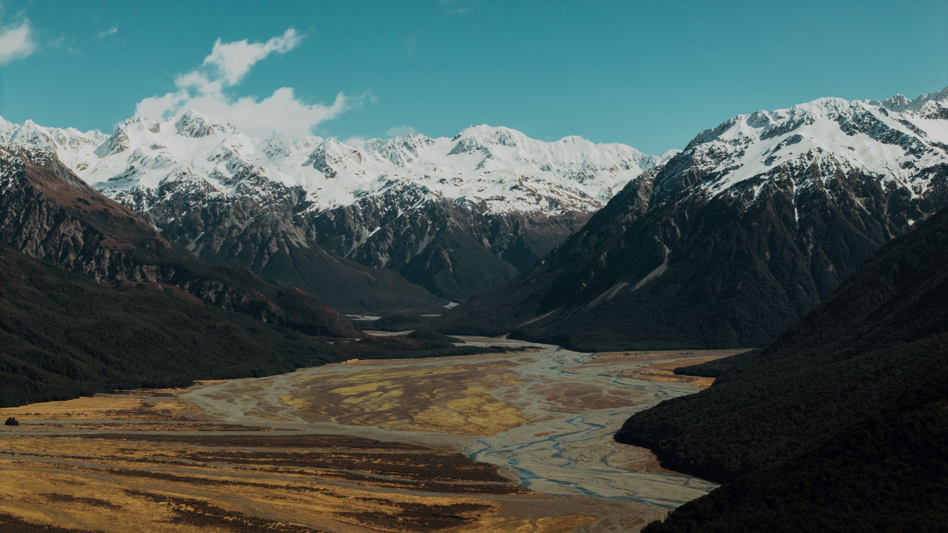 Clear river flowing through a high-altitude valley with snow-capped peaks in the background