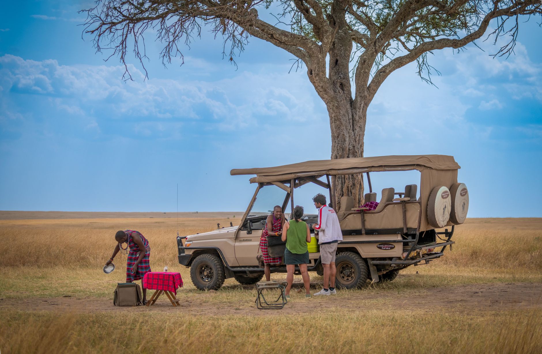 A tented safari camp set on a riverbank at dusk with firelight visible through canvas walls