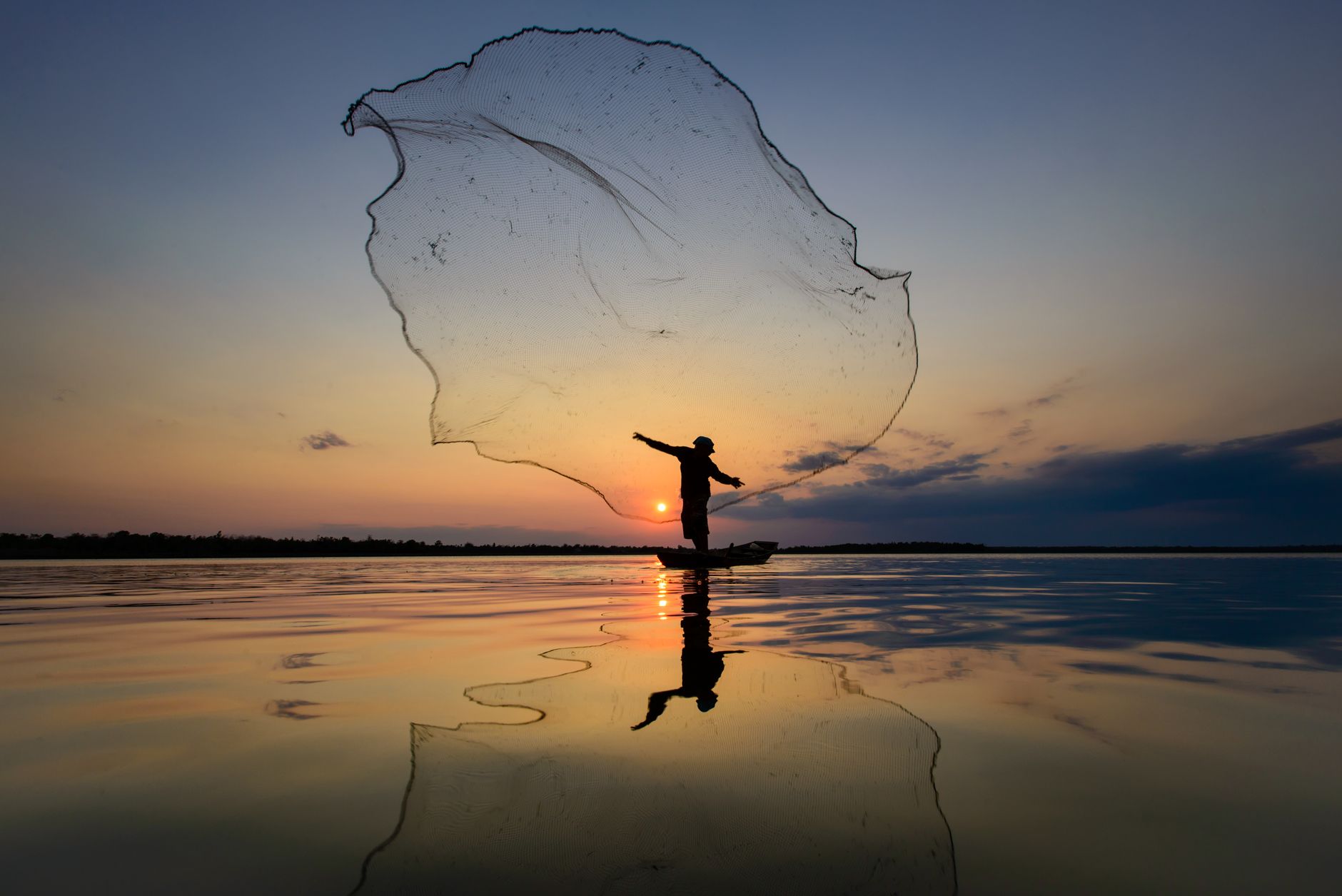 Silhouette of a fisherman casting a net on a still lake at sunrise